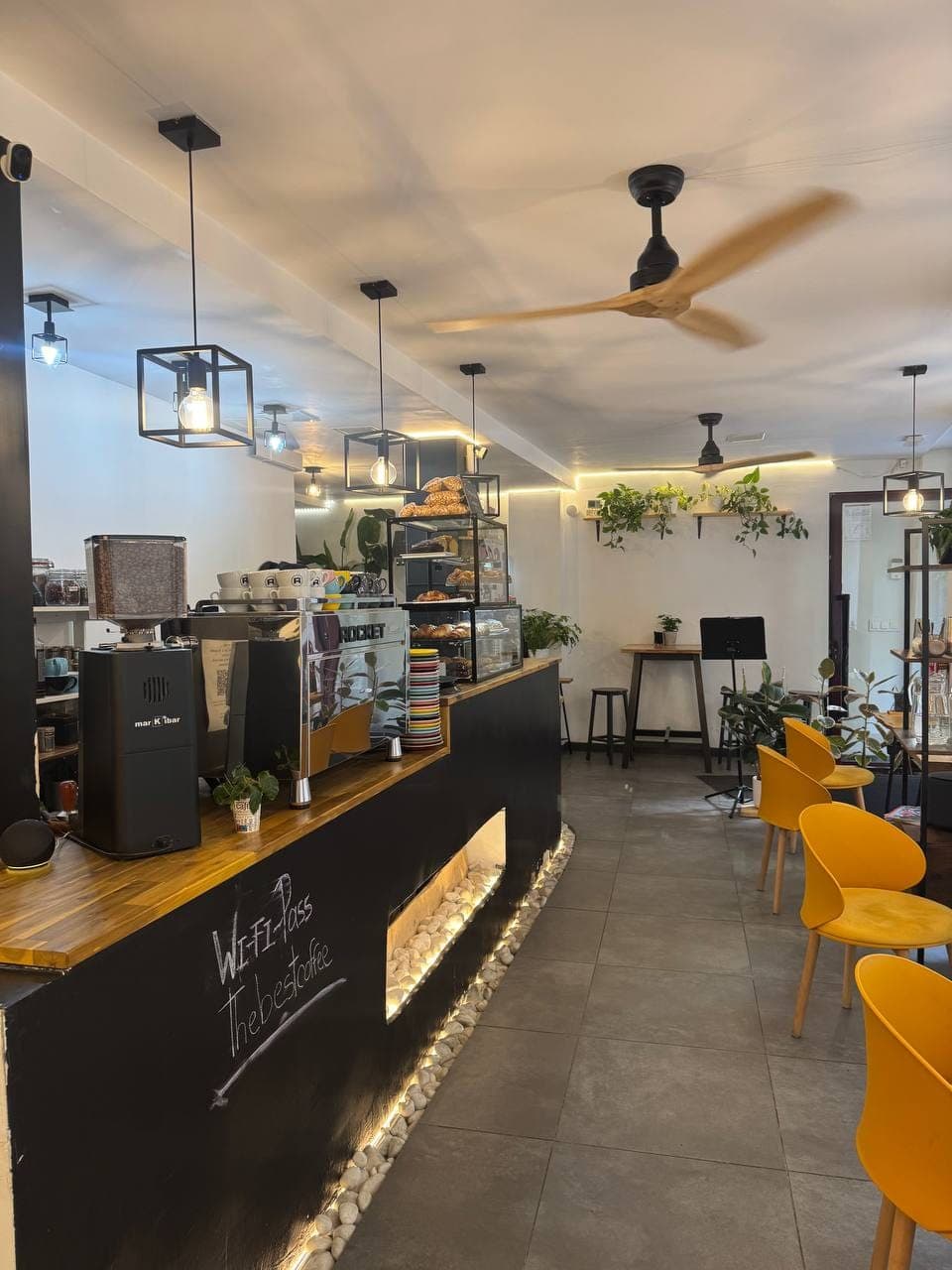 Barra de Baristas Club con máquina de café, tazas, plantas y zona de mesas